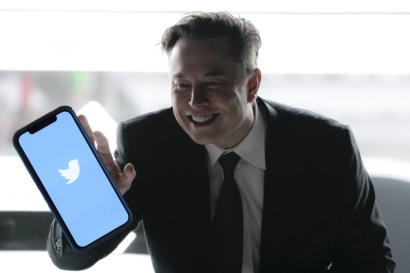 Elon Musk beugt sich über ein Handy mit Twitter-Logo