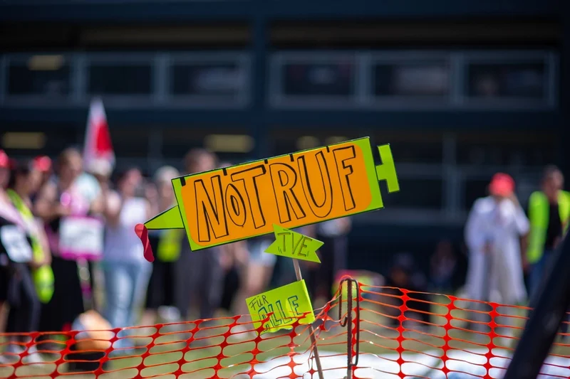 Demonstrationsplakat in Form einer Spritze mit der Aufschrift NOTRUF