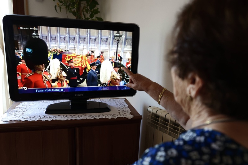 Ältere Frau sitzt vor Fernseher, auf dem das Begräbnis der Queen läuft