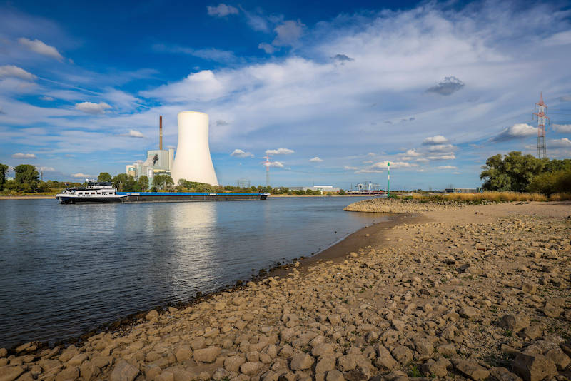 Ein Frachter auf dem wasserarmen Rhein, dahinter ein Kohlekraftwerk.