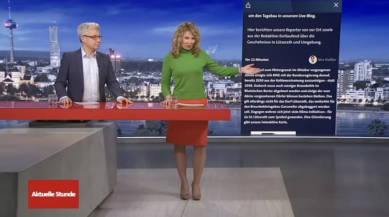 Moderatorin der "Aktuellen Stunde" im WDR zeigt auf den neben ihr eingeblendeten Lützerath-"Liveticker" des Senders.