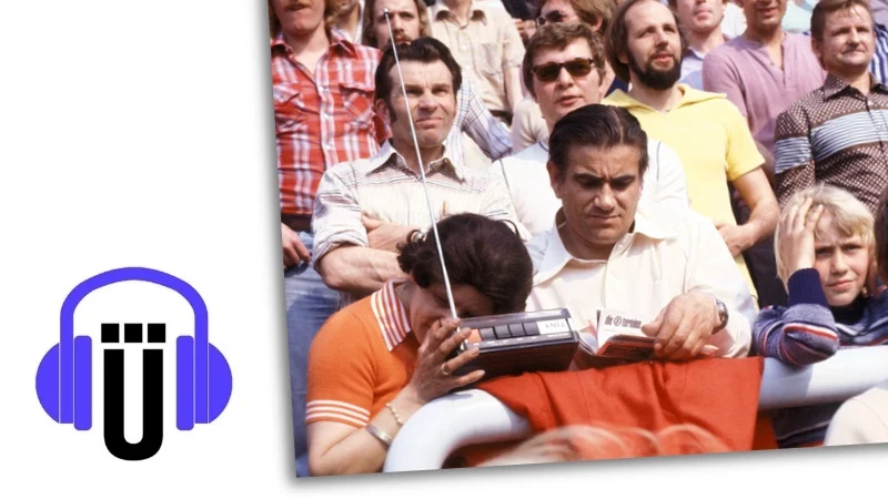 Foto einer Frau inmitten anderer Menschen in einem Stadion, die mit einem Ohr auf ihrem Transistorradio liegt.