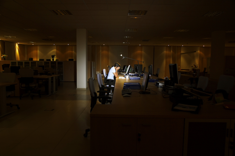 Verzweifelte Person, die einsam in einem dunklen Büro sitzt.