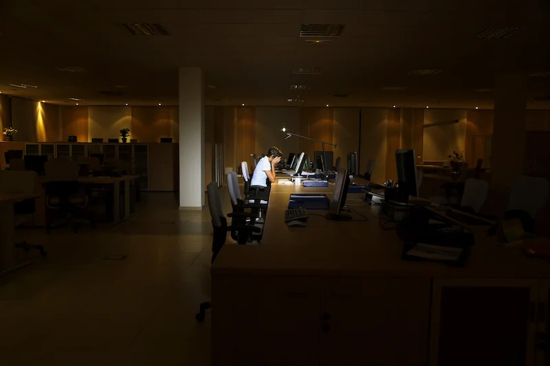 Verzweifelte Person, die einsam in einem dunklen Büro sitzt.