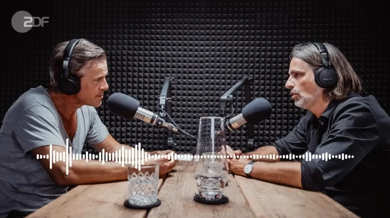 Markus Lanz (links) und Richard David Precht, beide mit Kopfhörern, sitzen sich in einem Studio an einem Tisch gegenüber.