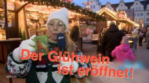 Eine NDR-Reporterin mit Mütze und Weihnachtspulli hat eine Tasse Glühwein in der Hand.