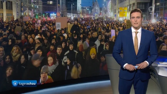 Constantin Schreiber in der „Tagesschau“ vor einem Bild von vielen Demonstranten