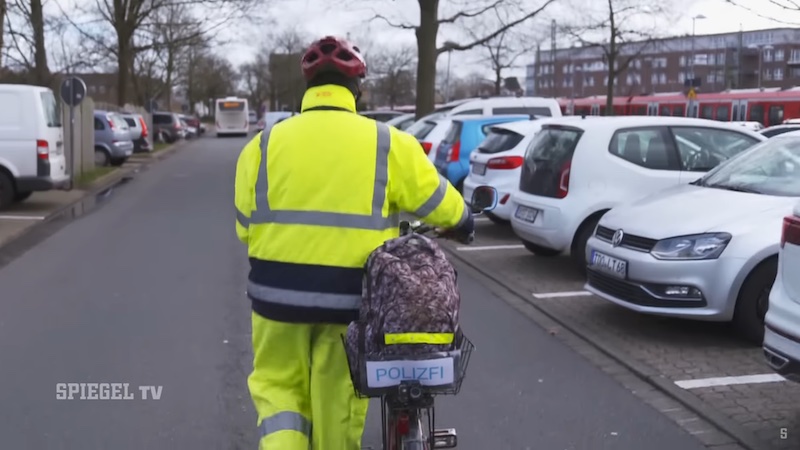 Screenshot aus dem "Spiegel-TV"-Film über den Anzeigenhauptmeister, der hier in gelber Montur sein Fahrrad schiebt.