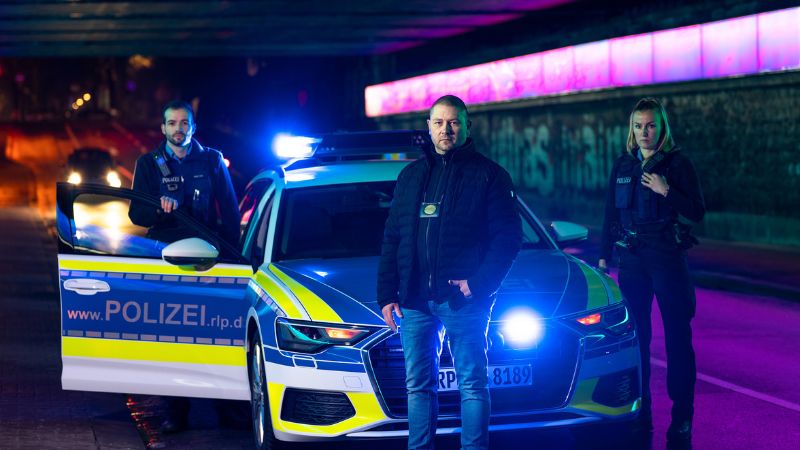 Drei Polizisten aus der SWR-Dokuserie "Nachtstreife" vor einem Polizeiwagen