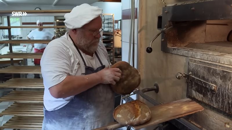 Bäcker mit Brot vor dem Ofen