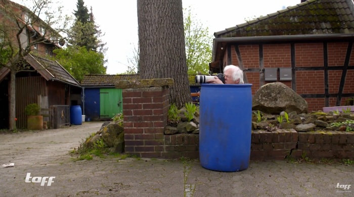 Hans Paul hockt in einer blauen Tonne, nur sein Kopf und seine Kamera schauen raus.