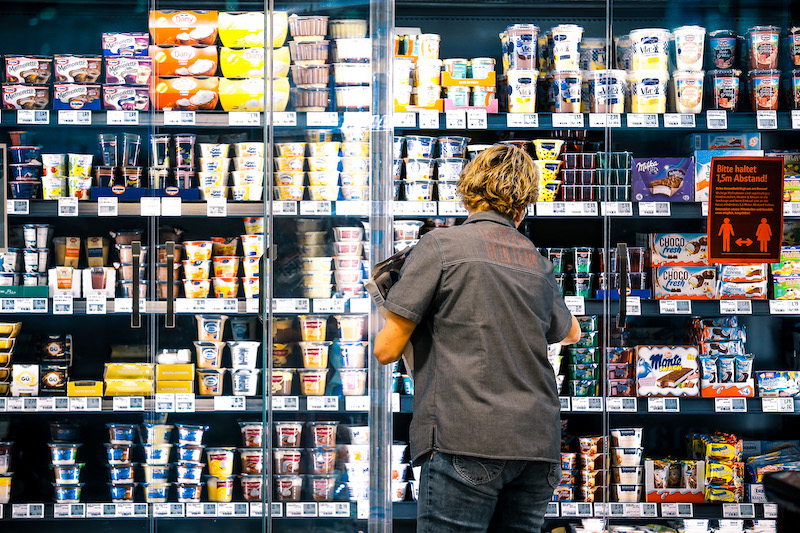 Mitarbeiterin eines Supermarkts beim Einräumen des Kühlregals