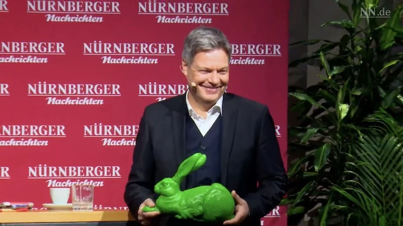 Robert Habeck lächelnd bei einer Veranstaltung der "Nürnberger Nachrichten". In der Hand hält er einen grünen Plastik-Hasen.