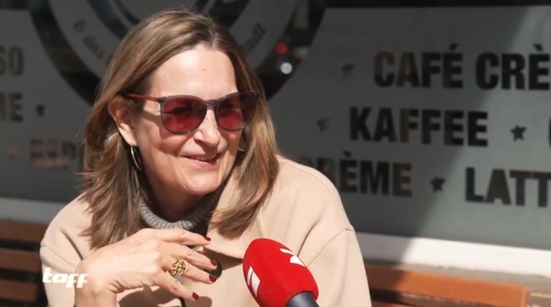 Brünette Frau mit Sonnenbrille vor einem Café, die in ein ProSieben-Mikrofon spricht.