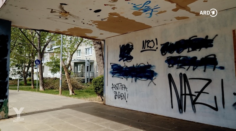 Szene aus "Y-Kollektiv"-Reportage: Eine Wand, an der unter anderem "Antifa jagen" und "Nazi" steht, dahinter sind Häuser zu erkennen.