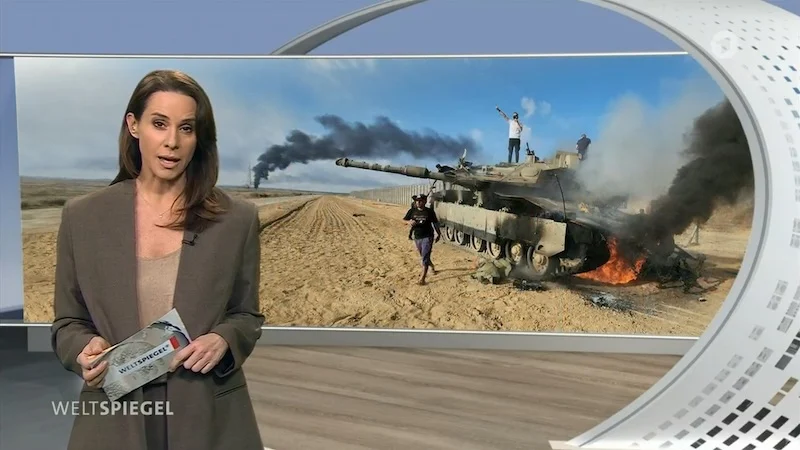 „Weltspiegel“-Moderatorin Natalie Amiri, im Hintergrund das Bild eines brennenden und rauchenden Panzers.