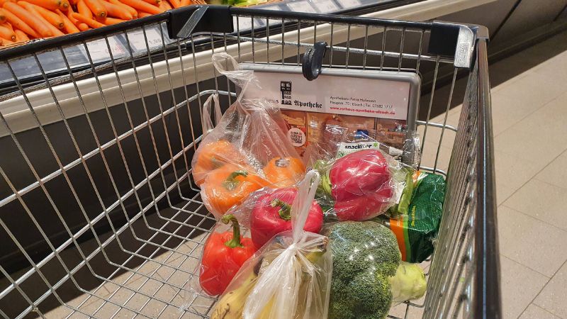 Blick in einen Einkaufswagen im Supermarkt mit in Plastik verpacktem Obst und Gemüse