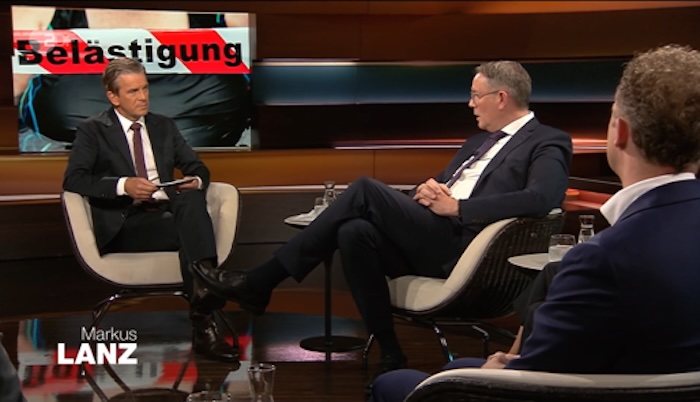 Talkrunde bei „Markus Lanz“, im Hintergrund: Nahaufnahme eines Frauenoberkörpers im Bikini, davor rot-weißes Flatterband mit der Aufschrift „Belästigung“.