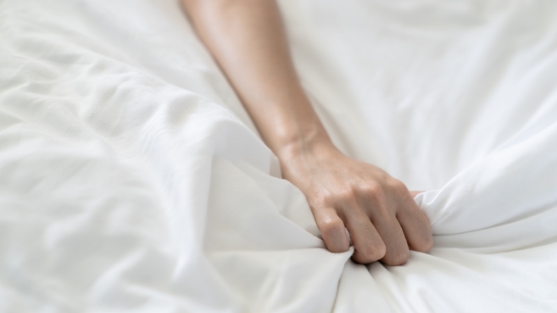 Frauenhand, die ins Bettlaken krallt