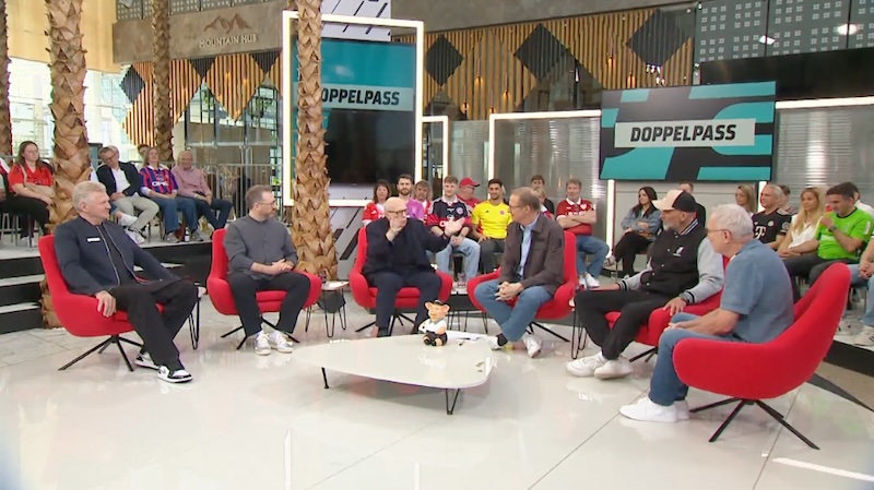 Sechs Männer in roten Sesseln: „Doppelpass“-Runde bei Sport 1. Reiner Calmund gestikuliert mit den Armen.