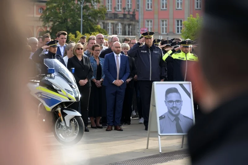 Mahnwache für den im saarländischen Völklingen getöteten Polizisten Simon Bohr im Sommer 2025: Hinter einem Aufsteller mit einem schwarz-weißen Foto des Polizisten stehen Personen und schweigen, darunter viele Polizisten.