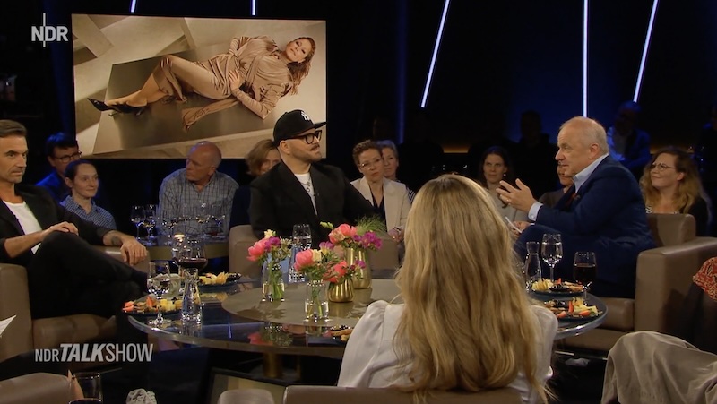 Armin Morbach und andere in der „NDR Talk Show“. Im Hintergrund auf einem Monitor ein Mugler-Werbemotiv, das Helene Fischer zeigt.