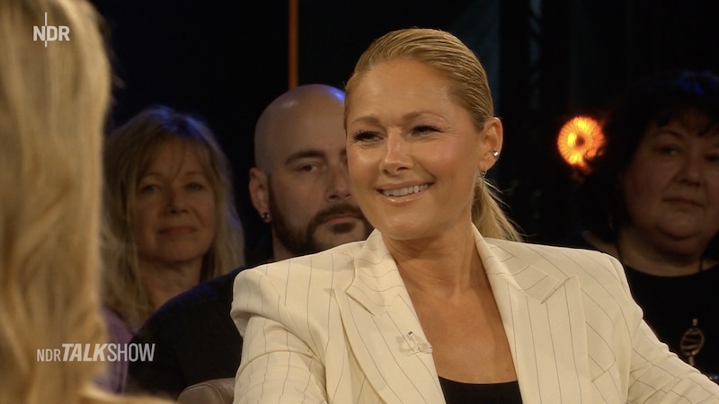 Helene Fischer grinsend und im weißen Nadelstreifenblazer in der „NDR Talk Show“.