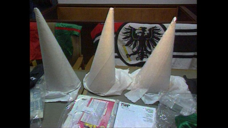 Vermeintliche Hüte des Ku-Klux-Klan auf einem Tisch, im Hintergrund eine Reichskriegsflagge. Der Filmemacher Michael Born hat sie als Requisiten für seine Fake-Reportagen benutzt.