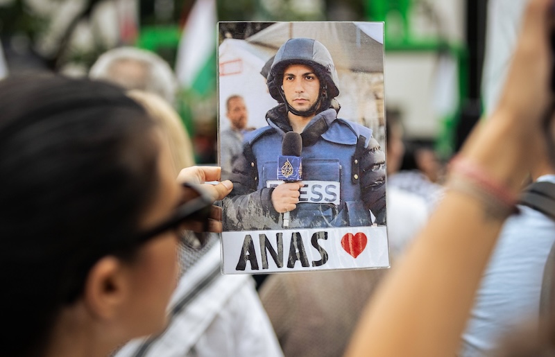 Eine Frau hält bei einer Demonstration ein Foto von Anas Al-Sharif hoch. Er trägt einen Helm und eine Schutzweste mit der Aufschrift „Press“.