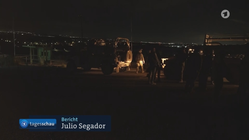 Militärfahrzeuge bei Nacht, im Hintergrund dunkle Hügel mit vereinzelten Lichtern