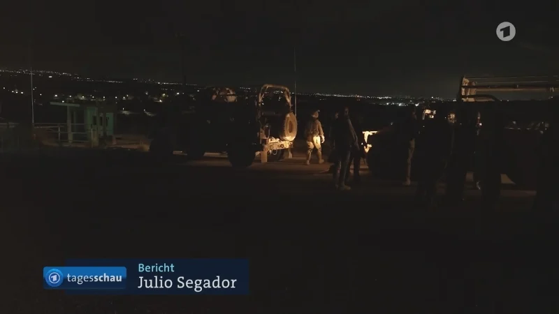 Militärfahrzeuge bei Nacht, im Hintergrund dunkle Hügel mit vereinzelten Lichtern