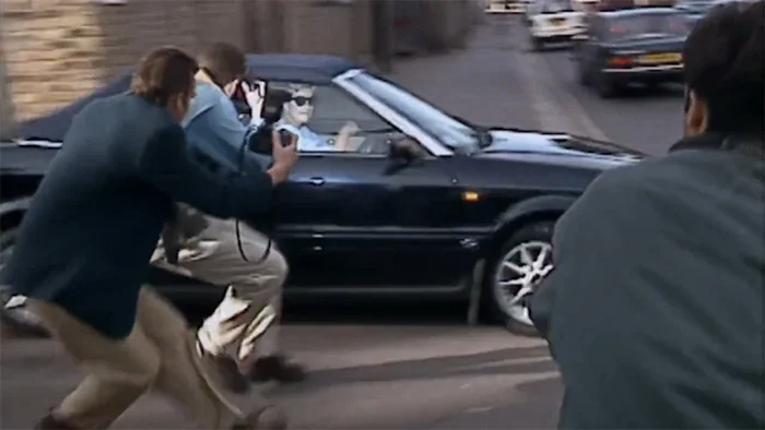 Prinzessin Diana sitzt in ihrem Auto, will wegfahren, als mehrere Paparazzi mit Kameras auf das Auto zustürmen.