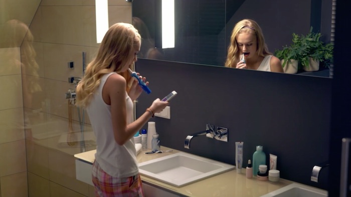 Standbild aus dem Imagefilm der Funke Mediengruppe: Eine Teenagerin steht im Bad, putzt sich die Zähne und liest dabei auf dem Smartphone.