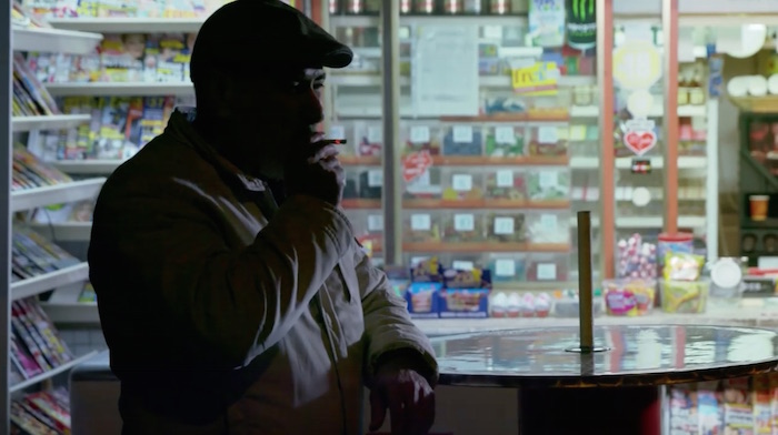 Standbild aus dem Imagefilm der Funke Mediengruppe: Ein Mann steht im Halbdunkel vor einem Kiosk und zieht an einer Zigarette.