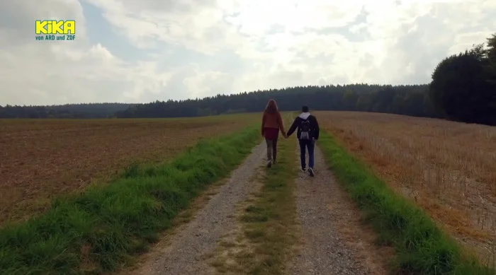 Ein junges Paar läuft Hand in Hand über einen Feldweg.