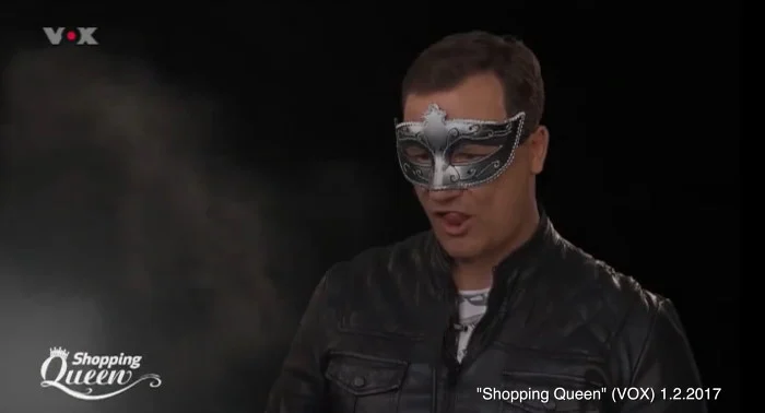 Guido Maria Kretschmer sitzt mit silberner Maske und Lederjacke vor der Kamera und streckt leicht die Zunge raus.