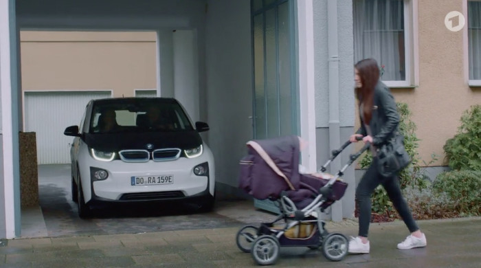 Szene aus der "Lindenstraße" (Das Erste) vom 30.4.2017. Zu sehen ist ein Auto, das aus einer Ausfahrt fährt, davor läuft eine Frau mit Kinderwagen.
