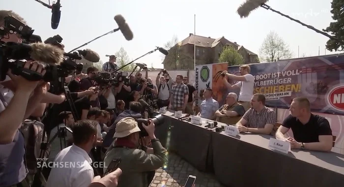 Dutzende Reporter scharen sich um einen langen Tisch, an dem Vertreter der NPD sitzen.