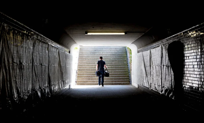 Ein Mann geht aus einem dunlen Tunnel heraus. Draußen ist Tag.