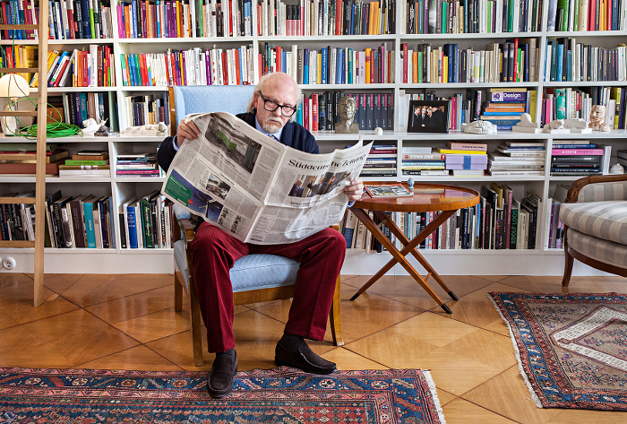 Sigmar Seelenbrecht sitzt in seiner Berliner Wohnung vor einer Bücherwand und liest Zeitung