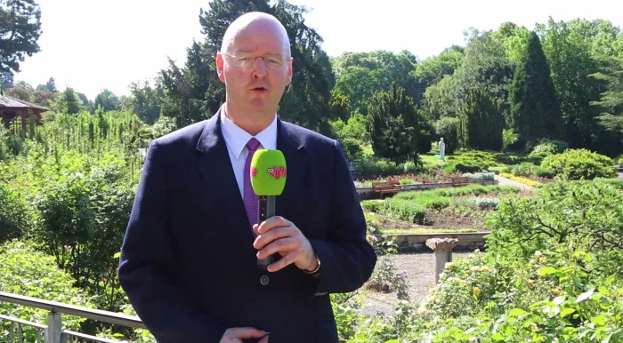Ein Mann steht im Anzug in einem weitläufigen Garten und spricht in ein Mikrofon des Senders "MDR Jump".