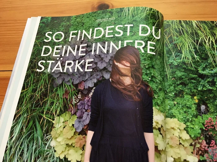 Frau steht vor einer grün beflanzten Wand, hat Haare vor dem Gesicht, daneben der Text: "So findest du deine innere Stärke"