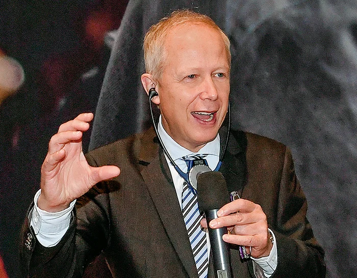 Blonder Mann im Anzug, der in ein Mikrofon spricht.