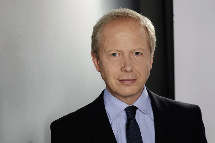 Mann mit blondem Haar und Anzug schaut in die Kamera.